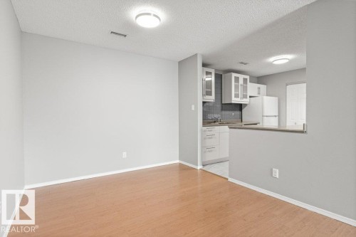 Wood-finish flooring, white cabinetry with clear panel inserts, grey tile backsplash, and light-colored countertops - #4 14620 26 St Nw, Edmonton, AB 