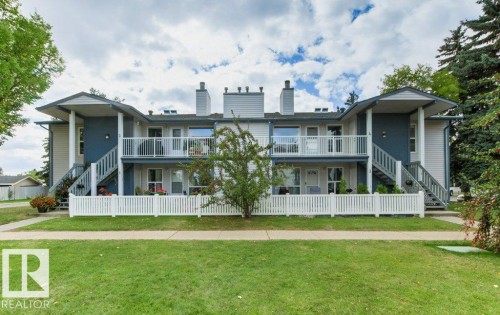 Two-story apartment building with light-colored siding, multiple balconies with white railings, and white picket fencing - #4 14620 26 St Nw, Edmonton, AB 