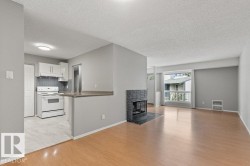 Wood-finish flooring, a contemporary fireplace with a dark stone surround, white kitchen cabinetry, a tile kitchen backsplash, and a breakfast bar - 