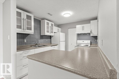 White cabinetry, glass-front upper cabinets, gray tiled backsplash, integrated sink, and a peninsula countertop - #4 14620 26 St Nw, Edmonton, AB 