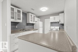 White cabinetry, glass-front upper cabinets, gray tiled backsplash, integrated sink, and a peninsula countertop - 