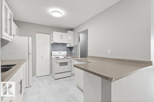 White cabinetry, laminate countertops, tile flooring, and integrated white appliances - #4 14620 26 St Nw, Edmonton, AB 