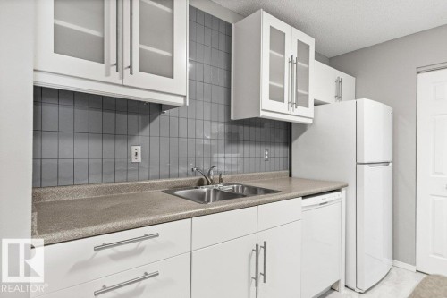 White cabinetry with frosted glass inserts, gray tile backsplash, double basin stainless steel sink, light-colored countertops, and white appliances - #4 14620 26 St Nw, Edmonton, AB 
