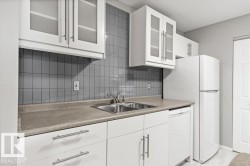 White cabinetry with frosted glass inserts, gray tile backsplash, double basin stainless steel sink, light-colored countertops, and white appliances - 