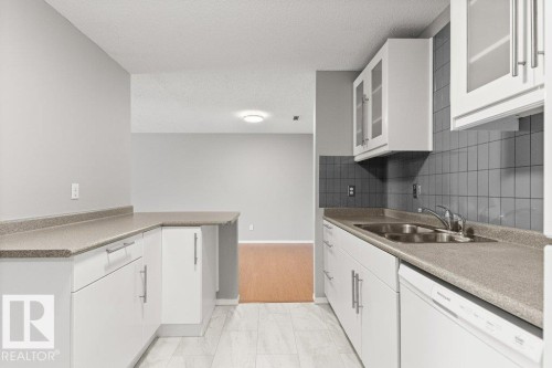 Kitchen featuring white cabinetry, grey countertops, grey tiled backsplash, a double basin sink, and wood-finish flooring in the adjacent area - #4 14620 26 St Nw, Edmonton, AB 