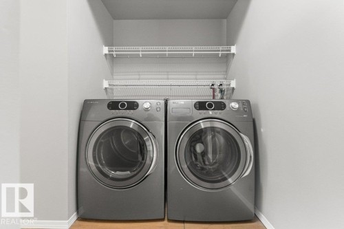 Dedicated laundry area featuring a front-loading washer and dryer set, integrated wire shelving, and light-toned walls - #4 14620 26 St Nw, Edmonton, AB 