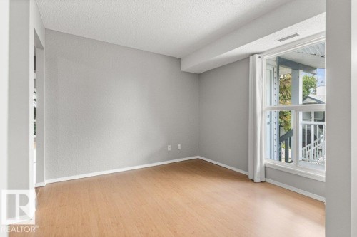 Light wood-finish flooring, neutral wall paint, and a large window providing natural light - #4 14620 26 St Nw, Edmonton, AB 