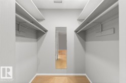 Walk-in closet featuring wood-finish flooring and multiple shelving units with hanging rods - 