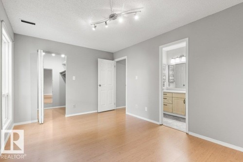 Wood-finish flooring, track lighting fixture, closet with bifold doors, window with white trim, and a three-panel interior door - #4 14620 26 St Nw, Edmonton, AB 
