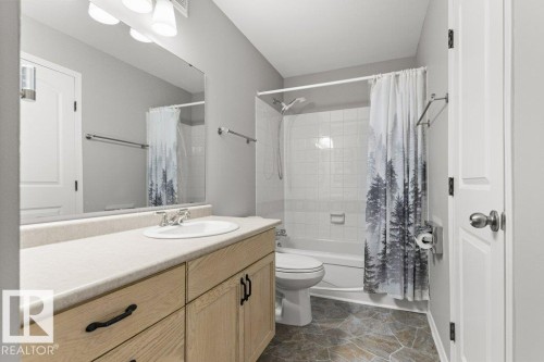 White porcelain bathtub with a shower, vanity with light wood-finish cabinetry, light-toned countertop, and a large wall-mounted mirror - #4 14620 26 St Nw, Edmonton, AB 
