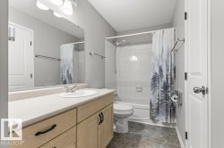 White porcelain bathtub with a shower, vanity with light wood-finish cabinetry, light-toned countertop, and a large wall-mounted mirror - 