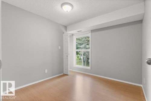 Wood-finish flooring with a neutral wall palette, featuring a window with white trim and a ceiling-mounted light fixture - #4 14620 26 St Nw, Edmonton, AB 