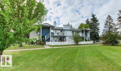 Multi-level exterior with balconies, featuring a white picket fence, mature trees, and a concrete walkway - #4 14620 26 St Nw, Edmonton, AB 