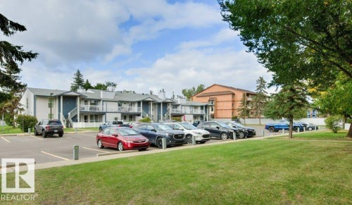 Surface parking lot with painted space lines, surrounded by manicured green space and mature trees - #4 14620 26 St Nw, Edmonton, AB 