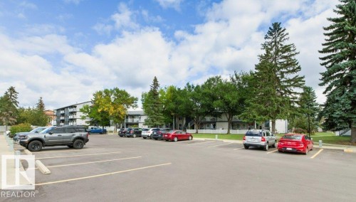 Paved parking lot with designated spaces, bordered by mature trees and landscaping - #4 14620 26 St Nw, Edmonton, AB 