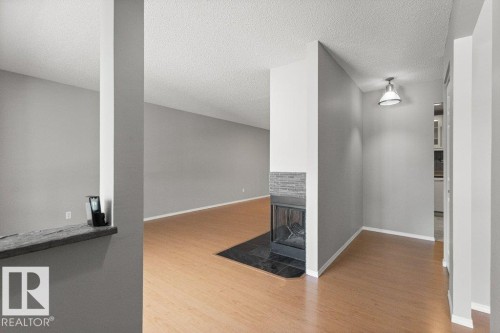 Wood-finish flooring throughout, complemented by a stone-faced fireplace with a black hearth - #4 14620 26 St Nw, Edmonton, AB 