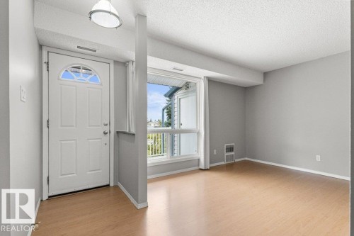 Entry door with arched transom window, wood-finish flooring, crisp white trim, and a prominent window - #4 14620 26 St Nw, Edmonton, AB 