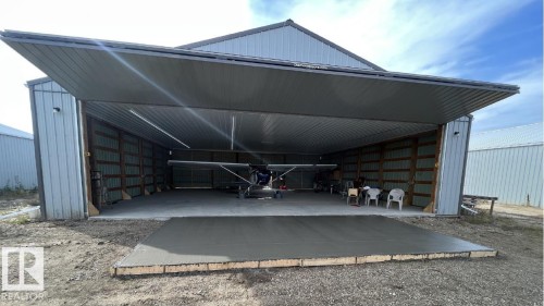 Metal-clad building featuring a large hydraulic door, concrete flooring, exposed wood framing, and fluorescent lighting - 26453 Twp Rd 481, Rural Leduc County, AB 