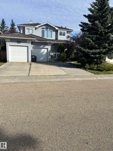 Stucco exterior with a peaked roofline, two integrated garages, a large arched window feature, and established landscaping - 566 Butterworth Way Nw, Edmonton, AB 