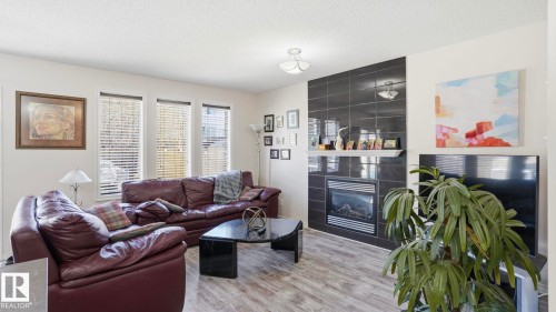 Living area featuring wood-finish flooring, a contemporary ceiling light fixture, and multiple windows with blinds - 1709 64 Street Sw, Edmonton, AB 