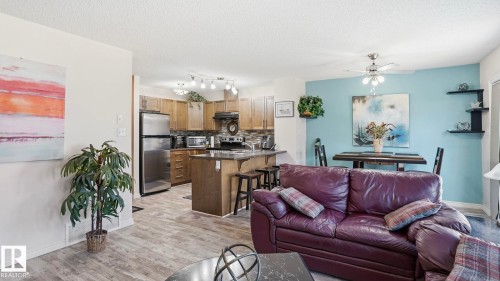 Open-concept living space featuring wood-finish flooring, a kitchen island with seating, stainless steel appliances, and a dining area with a ceiling fan - 1709 64 Street Sw, Edmonton, AB 