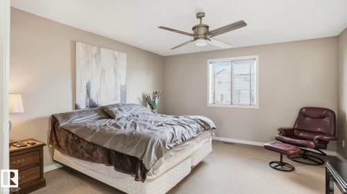 Neutral wall tones, carpeted flooring, a ceiling fan with integrated lighting, and a large window providing natural illumination - 1709 64 Street Sw, Edmonton, AB 