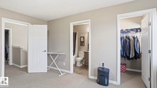 Carpeted room with a doorway to a full bathroom, a closet with built-in shelving, and a separate doorway to a hallway with stairs - 1709 64 Street Sw, Edmonton, AB 