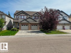 Duplex exterior with attached two-car garage, stone veneer accents, and a paved driveway - 