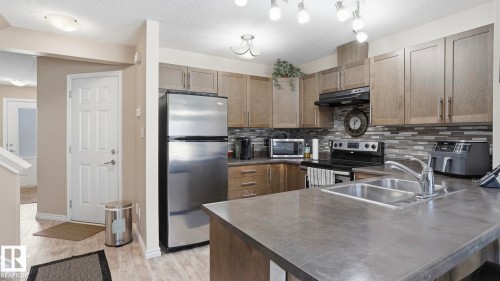 Kitchen featuring wood-finish cabinetry, stainless steel appliances, a tile backsplash, and a double basin sink - 1709 64 Street Sw, Edmonton, AB 