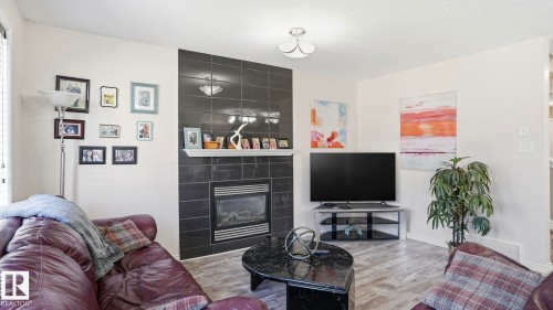 Fireplace with dark tile surround and white mantel, wood-finish flooring, and a flush mount ceiling light fixture - 1709 64 Street Sw, Edmonton, AB 