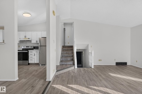 Wood-finish flooring throughout, vaulted ceilings, white kitchen cabinetry with stainless steel appliances, and a carpeted staircase with a white railing - 3722 34A Avenue Nw, Edmonton, AB 
