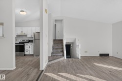 Wood-finish flooring throughout, vaulted ceilings, white kitchen cabinetry with stainless steel appliances, and a carpeted staircase with a white railing - 