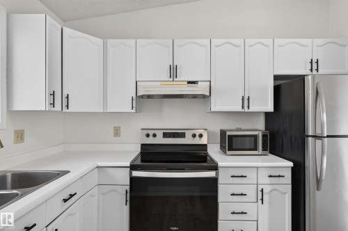 White cabinetry with black hardware, stainless steel sink, white countertops, and stainless steel appliances - 3722 34A Avenue Nw, Edmonton, AB 