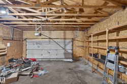 Garage space featuring exposed wood trusses, an automatic garage door opener, wood-finish walls, concrete flooring, and built-in wood shelving - 