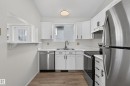 Updated kitchen with white cabinetry, stainless steel appliances, wood-finish flooring, and a pass-through window - 3722 34A Avenue Nw, Edmonton, AB 
