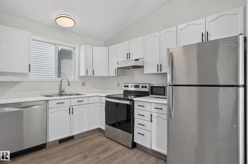 Kitchen featuring white cabinetry with dark hardware, stainless steel appliances, wood-finish flooring, and a ceiling-mounted light fixture - 3722 34A Avenue Nw, Edmonton, AB 