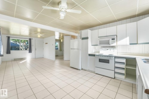 Open-concept living space featuring ceramic tile flooring, ceiling fans, and a kitchen with white cabinetry, built-in microwave, and an electric range - 11841 71 Street Nw, Edmonton, AB 
