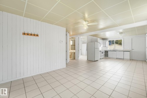 Tile flooring throughout, white vertical plank wall paneling, ceiling fan, white kitchen cabinetry, and large kitchen window - 11841 71 Street Nw, Edmonton, AB 