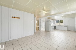 Tile flooring throughout, white vertical plank wall paneling, ceiling fan, white kitchen cabinetry, and large kitchen window - 