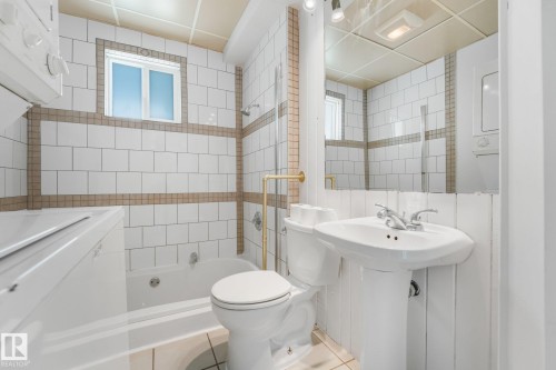 Bathroom featuring a pedestal sink, white subway tile with accent banding, a window, and a built-in tub with shower - 11841 71 Street Nw, Edmonton, AB 