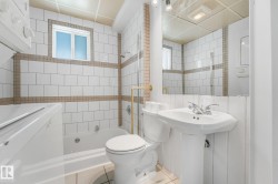 Bathroom featuring a pedestal sink, white subway tile with accent banding, a window, and a built-in tub with shower - 