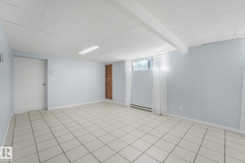 Expansive room featuring light-toned tile flooring, light-colored walls, and a suspended ceiling - 11841 71 Street Nw, Edmonton, AB 