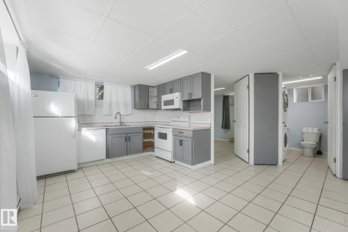 Tile flooring, gray cabinetry, white appliances, integrated sink, and a stacked washer and dryer - 11841 71 Street Nw, Edmonton, AB 