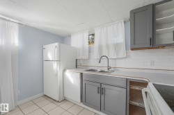 Tile flooring, white subway tile backsplash, dual basin stainless steel sink, light gray lower cabinetry, and light gray upper cabinetry - 