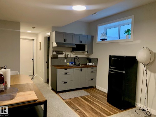 Compact kitchen featuring gray cabinetry, wood-finish countertops, stainless steel sink, and a black refrigerator - 9111 65 Avenue Nw, Edmonton, AB 