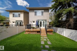 Spacious backyard featuring a manicured lawn, stone paver pathway, and a large wooden deck with black railings - 