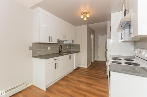 Kitchen featuring white cabinetry with dark hardware, a grey subway tile backsplash, dark countertops, and wood-finish flooring - Edmonton, AB - Indoor Photo Showing Kitchen