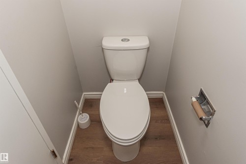Powder room featuring a white two-piece toilet, wood-finish flooring, light gray walls, white trim, and a recessed toilet paper holder - Edmonton, AB - Indoor