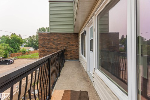 Concrete balcony with black metal railing, featuring a white door and large window - Edmonton, AB - Outdoor With Exterior