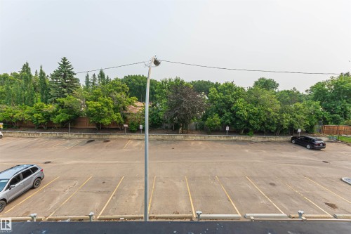 Paved parking area with marked spaces, bordered by mature trees and a wood fence - Edmonton, AB - Outdoor